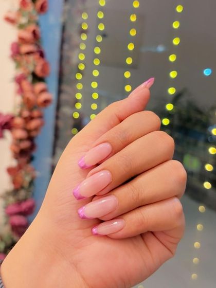 Pink chrome French tips seen against a festive, fairy-lit background.