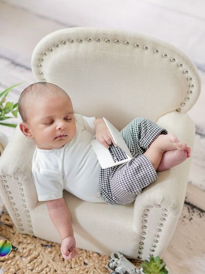 Even the smallest ones need a break. This playful shot captures a newborn "napping" in a miniature armchair after a long day of being cute.