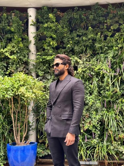 A side profile of Allu Arjun's London look. The clean lines of the suit stand out against the lush green background, showcasing the power of a well-tailored piece.