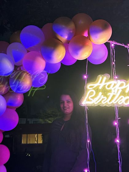 A simple yet beautiful outdoor birthday setup with a balloon arch and neon sign, perfect for an evening celebration.