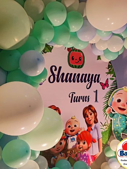 A close-up of a Cocomelon-themed first birthday backdrop, surrounded by a soft green and white balloon garland.