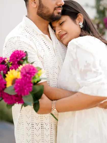 A tender embrace filled with warmth and comfort. The woman holds a vibrant bouquet while resting her head on her partner's chest, a beautiful, quiet moment from their pre-wedding session.