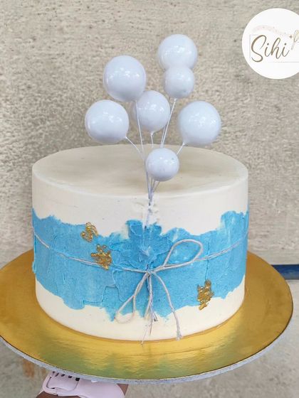A minimalistic anniversary cake with a textured blue watercolor effect. The design is finished with a simple twine bow and a bunch of white bauble balloons.
