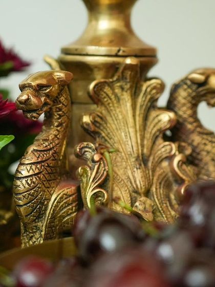A close-up of an antique brass prop with intricate dragon carvings, surrounded by deep red flowers and fresh cherries.
