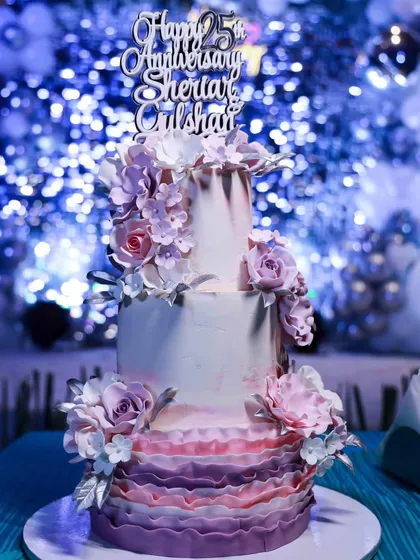 A slightly different angle of the lavender ombre 25th-anniversary cake, highlighting the texture of the ruffles and the arrangement of the sugar flowers.