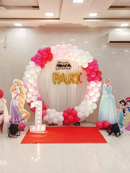 A grand princess-themed first birthday for Pari. This decoration features a circular balloon arch and cutouts of various Disney princesses and Barbie.