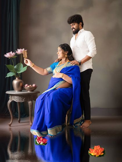 A creative studio shot where the mom-to-be in a blue saree holds a mirror, with her partner standing behind her, creating a reflective and artistic portrait.