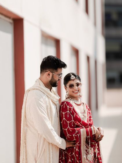 A cool and stylish portrait of the couple. The bride's sunglasses add a fun, modern twist to her traditional red attire, showing their playful personalities.