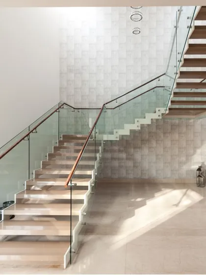 The staircase in this home is a sculptural element. The floating wooden treads and glass balustrade create a sense of lightness, allowing sunlight from above to filter down and illuminate the grand entrance hall.