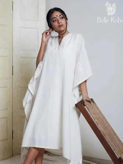 A serene and minimalist look for a daytime event. The model wears a simple white kaftan, and the makeup is equally understated, with a focus on natural beauty, a small bindi, and clean skin.