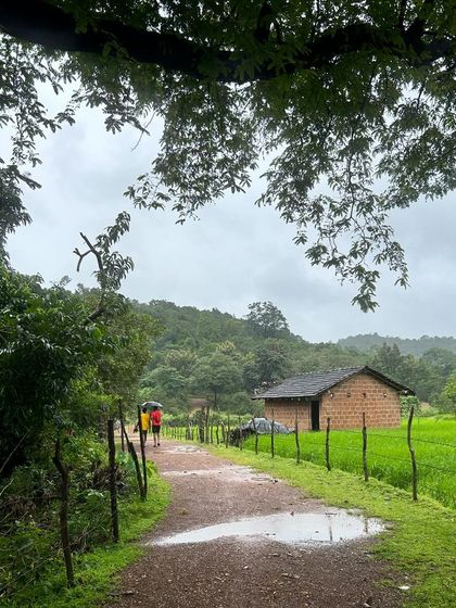 A walk through a village in the monsoon, with a traditional mud-walled house and green paddy fields creating a picturesque scene.