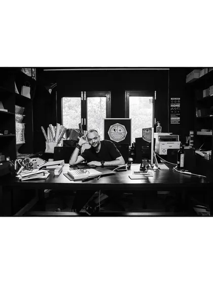 A wide shot of artist Pushkar Thakur in his studio, surrounded by his work. This black and white environmental portrait tells the story of his creative world.