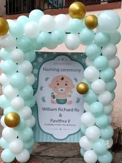An outdoor welcome sign for a naming ceremony, with a pastel blue and white balloon arch around a personalized invitation board.