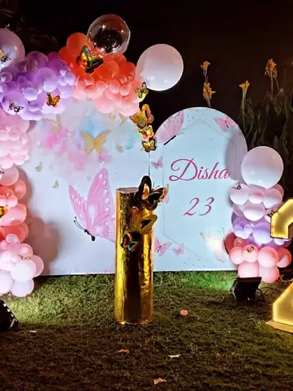An outdoor butterfly-themed setup for a 23rd birthday, featuring a balloon arch, marquee numbers, and a custom backdrop.