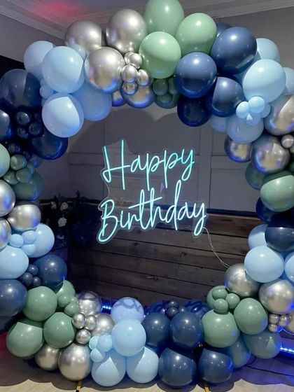 A stylish balloon ring in shades of blue, green, and silver, with a "Happy Birthday" neon sign.