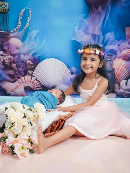 A big sister proudly sits with her newborn sibling in a magical, sea-themed setting.