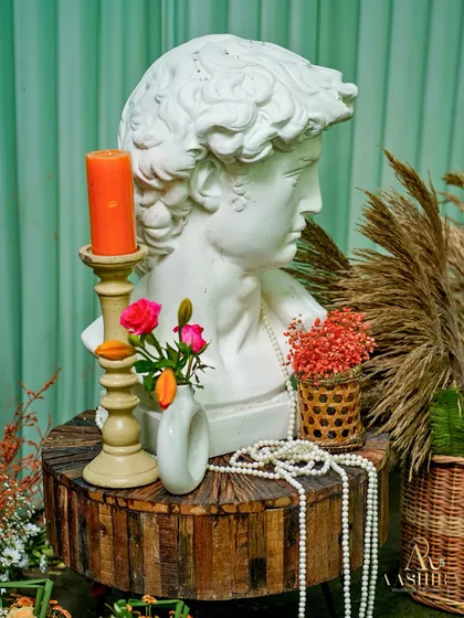 A curated corner where classical art meets rustic charm, with a statue bust, pearls, and dried grasses on a wooden pedestal.