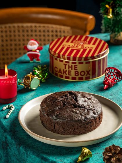 A classic Christmas fruit cake in a tin box, styled with a candle and ornaments to evoke a warm, festive feeling.