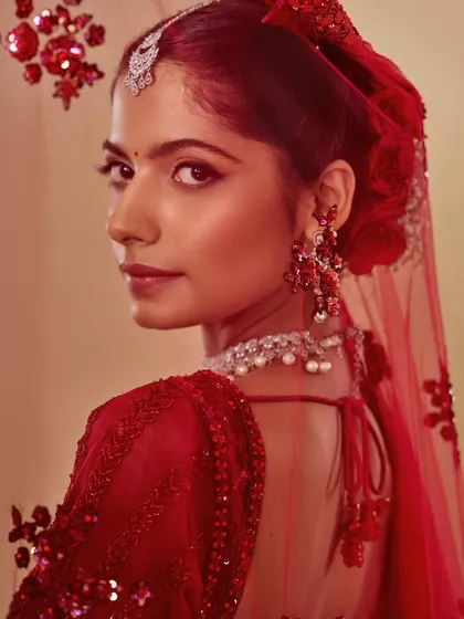 The quintessential red bride, looking over her shoulder. The makeup is classic and clean, with a defined eye and balanced lip, allowing the stunning red outfit and jewelry to shine.