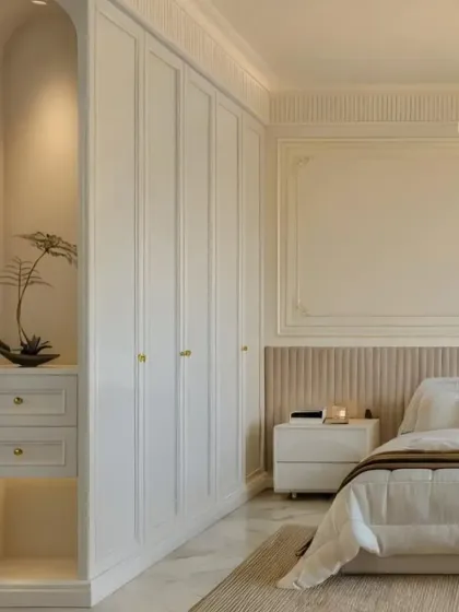 A serene and classic bedroom design in white and beige. The built-in wardrobe with arched details and a cozy niche adds a touch of architectural elegance.