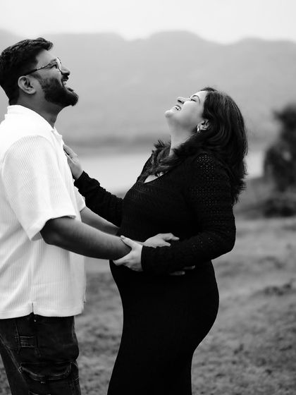 A black and white photo bursting with joy. The couple shares a hearty laugh by the lake, a perfect candid moment showing their happiness.