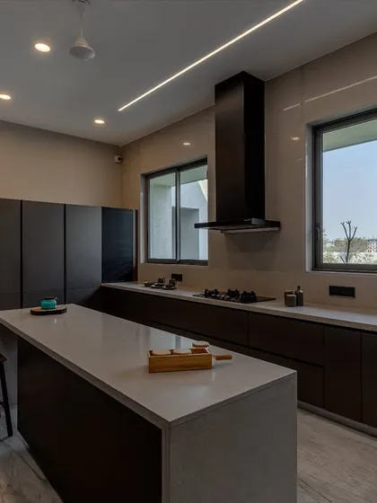 The kitchen is designed to be bright and airy, with large windows that flood the space with daylight. The dark cabinetry is balanced by a light countertop and flooring.