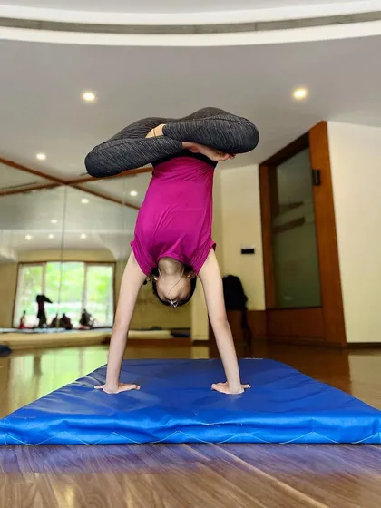 An impressive handstand with legs in a lotus position. This advanced pose requires immense core strength and balance, showcasing the high level of skill our students can achieve.