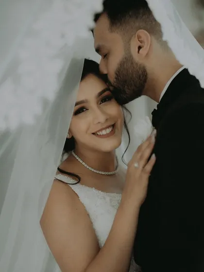 A close, intimate portrait of the groom kissing his bride's forehead under the soft light of her veil.