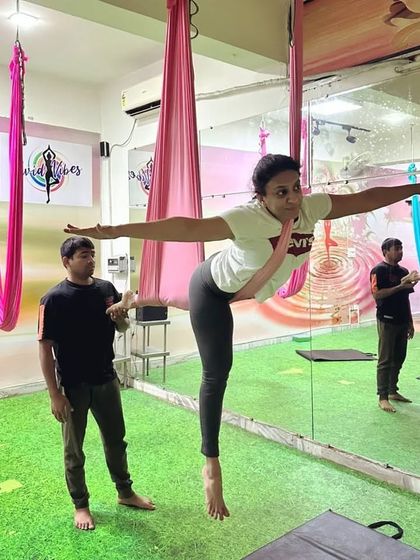 An instructor provides gentle guidance to help a student find the correct alignment in an aerial warrior pose. This support is crucial for preventing injury and getting the most out of each posture.