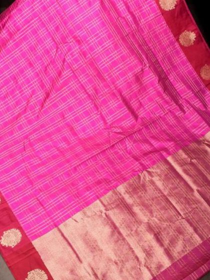 A bright pink checked silk saree with a rich red border. The gold buttas on the border add a touch of traditional opulence.