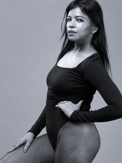 A close-up monochrome portrait of a model in a black bodysuit. The shot focuses on her confident expression and the clean lines of the outfit.