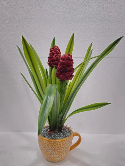 A unique artificial plant with red cone-like flowers and long green leaves, presented in a fun, mug-shaped yellow pot.