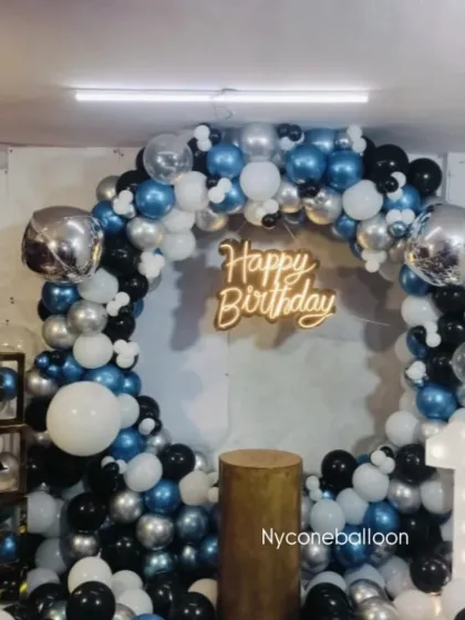 A classic ring decoration for a first birthday party. The blue, black, silver, and white balloons create a stylish look, complemented by a light-up number '1' and transparent letter blocks.