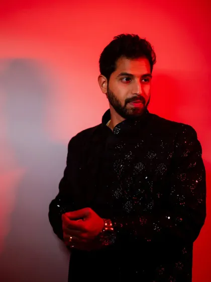 A stylish portrait of the groom against a dramatic red-lit background. His confident pose in a black, sequined sherwani creates a modern and sophisticated look.