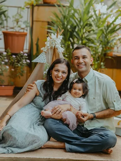 A wider view of the half-birthday celebration, showing the family seated comfortably in their beautifully decorated outdoor space, creating a relaxed and personal family portrait.