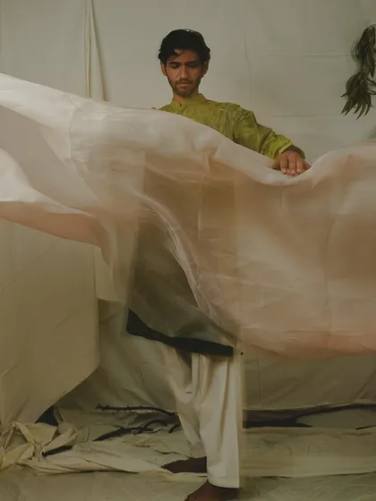 An artistic menswear shot where the model interacts with a flowing piece of sheer fabric. This creative approach adds movement and a sense of softness to the image, elevating it beyond a simple product shot.