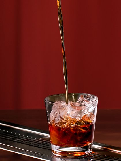 The perfect pour. A stream of rich, dark liquor cascades over ice, a simple yet satisfying moment in the creation of a classic cocktail on the rocks.