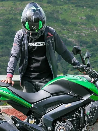 A rider posing with his green Dominar, with the lush green hills providing a perfect backdrop for a motorcycle photo.