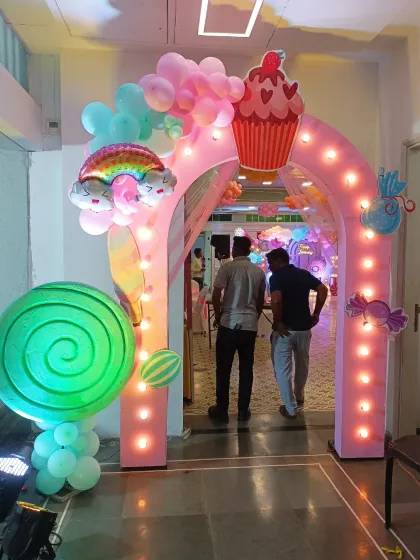 A whimsical lighted entrance arch for a Candyland party. Decorated with a giant lollipop, cupcake, and rainbow, it creates a sweet welcome for all the guests.