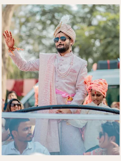 The groom's grand entrance during the baraat. His joyful wave and stylish pink sherwani capture the high energy and celebratory spirit of the procession.