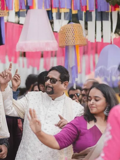 Guests dancing with abandon during the Baraat at a vibrant destination wedding. The colorful overhead decor with ribbons and cane baskets added to the festive atmosphere.