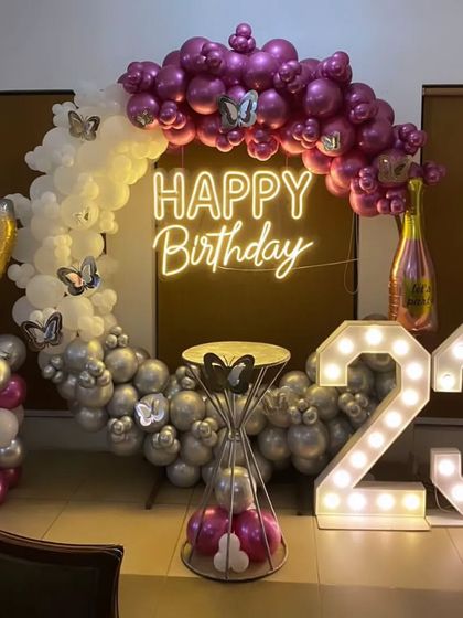 A glamorous 23rd birthday setup with a purple and silver balloon ring, butterfly accents, champagne-themed props, and marquee numbers.