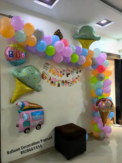 A delicious-looking Ice Cream theme birthday decoration. The pastel balloon arch is decorated with foil balloons shaped like ice cream cones, an ice cream truck, and a birthday cake.