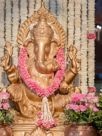 A golden Ganesha idol, adorned with a pink floral garland, sits at the entrance to bless the event. This is a crucial element for an auspicious beginning.