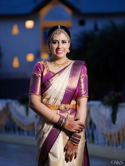 A change of saree for the same bride, showcasing a beautiful purple and off-white Kanjivaram. The makeup look transitions perfectly.