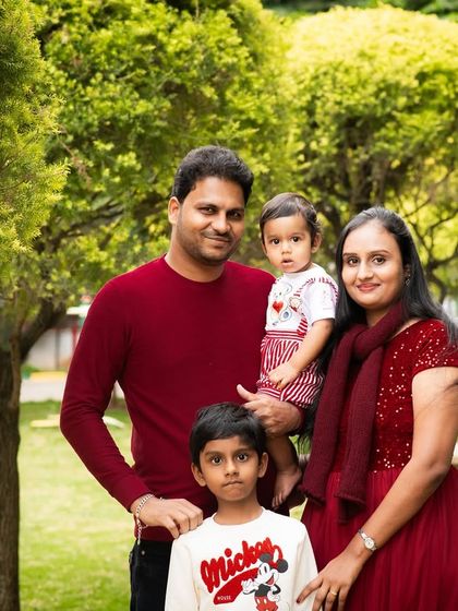 A lovely family portrait taken outdoors. The coordinated red outfits tie the family together visually, creating a warm and unified photograph.