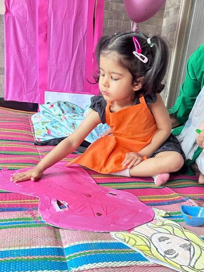A toddler exploring textures by painting a large Barbie dress cutout. This activity is great for sensory development and color recognition.