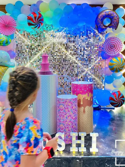 A young guest admiring the Candyland setup. The decor features plinths designed to look like ice cream and candy, set against a shimmering backdrop and framed by a colorful balloon arch.