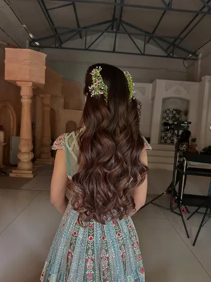 For a soft and romantic look, I styled this client's long hair in flowing, voluminous waves. The half-updo is subtly accented with delicate fresh flower clips, making it an ideal choice for an engagement, Mehendi, or outdoor wedding event.