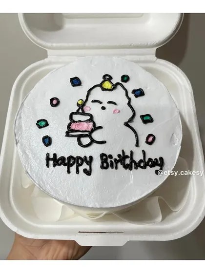 A whimsical birthday bento cake featuring a cute character holding a mini cake, surrounded by colorful confetti.